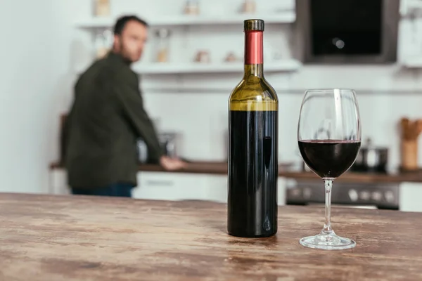 Enfoque selectivo de copa de vino con botella en la mesa y hombre en la cocina - foto de stock