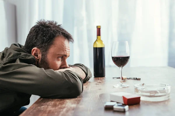 Foco seletivo do homem dependente de álcool olhando para o copo de vinho na mesa — Fotografia de Stock