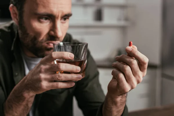 Selective focus of man with alcohol depended holding whiskey glass and pill — Stock Photo