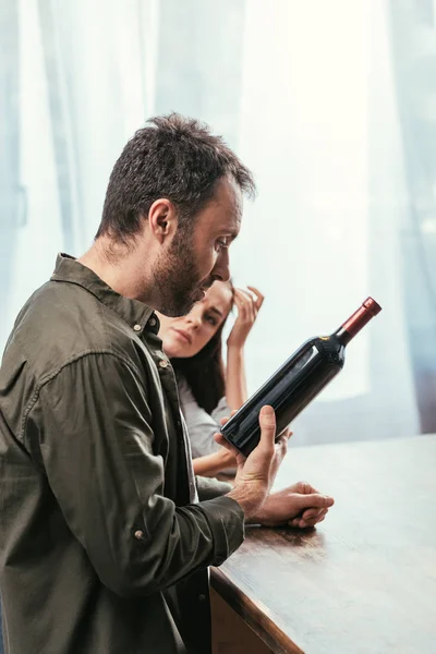 Enfoque selectivo del hombre con botella de vino y esposa preocupada en casa - foto de stock
