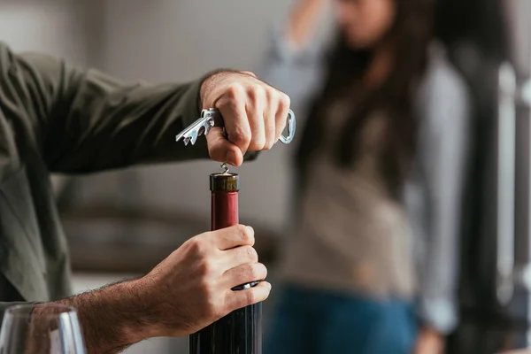 Selective focus of man opening wine bottle and worried wife at background — Stock Photo