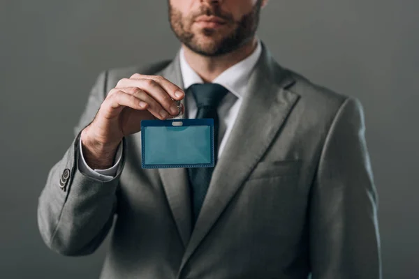 Cropped view of man in suit holding badge isolated on grey — Stock Photo