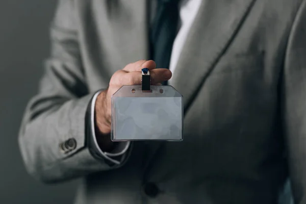 Cropped view of man in suit holding badge isolated on grey — Stock Photo