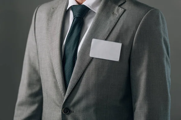 Обрезанный вид человека в костюме со значком, изолированным на сером — стоковое фото