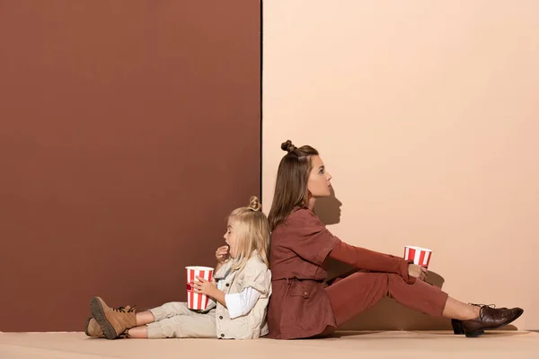 Back to back vista di figlia mangiare popcorn e attraente madre su sfondo beige e marrone — Foto stock