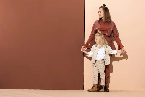 Nette Tochter und attraktive Mutter halten Händchen auf beigem und braunem Hintergrund — Stockfoto
