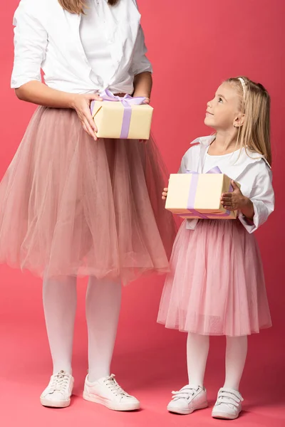 Cropped view of mother holding gift and smiling daughter looking at her on pink background — Stock Photo