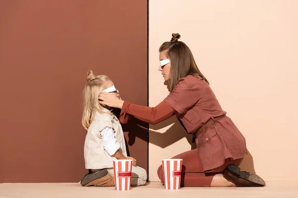 Vista lateral da mãe vestindo óculos 3d na filha em fundo bege e marrom — Fotografia de Stock