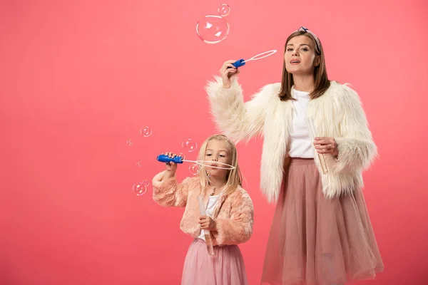 Fille et mère souriante soufflant des bulles de savon sur fond rose — Photo de stock