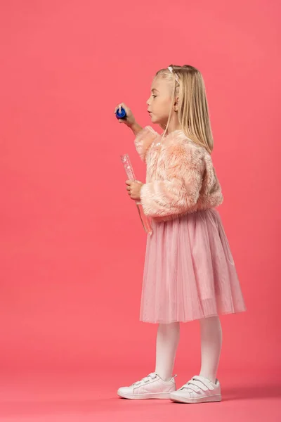 Side view of cute kid blowing soap bubbles on pink background — Stock Photo