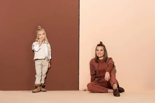 Pensive daughter and smiling mother looking at camera on beige and brown background — Stock Photo
