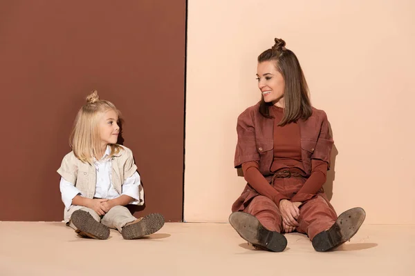 Sonriente hija y madre mirándose el uno al otro sobre fondo beige y marrón - foto de stock