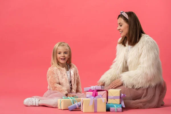 Sorrindo filha e mãe sentados perto de presentes no fundo rosa — Fotografia de Stock