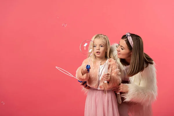 Daughter and smiling mother blowing soap bubbles isolated on pink — Stock Photo