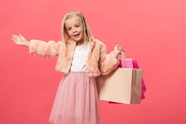 Sonriente y lindo niño sosteniendo bolsas aisladas en rosa - foto de stock