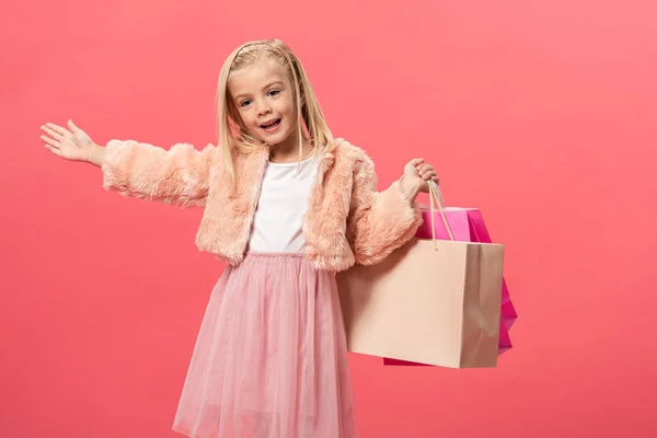 Enfant souriant et mignon tenant des sacs à provisions isolés sur rose — Photo de stock