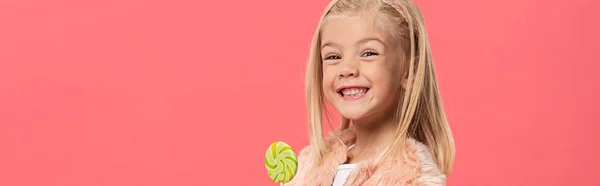 Plano panorámico de niño sonriente y lindo sosteniendo piruleta aislado en rosa - foto de stock