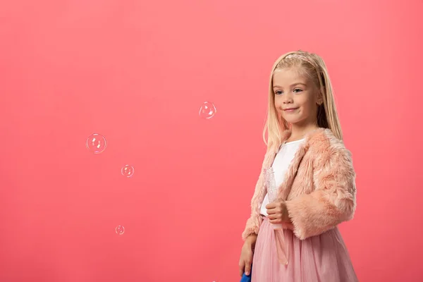 Cute and smiling kid holding bottle with soap bubbles isolated on pink — Stock Photo