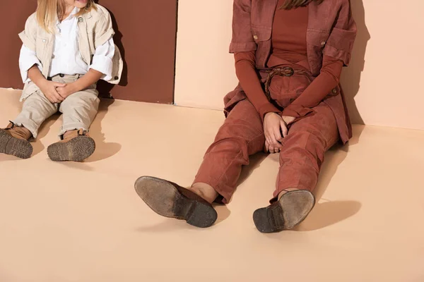 Vista recortada de la elegante hija y la madre sentado sobre fondo beige y marrón - foto de stock