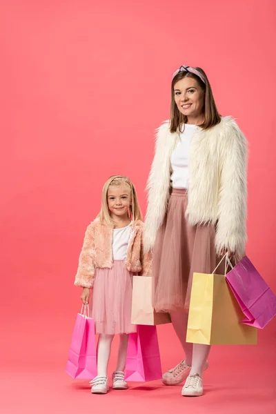 Smiling daughter and mother holding shopping bags on pink background — Stock Photo