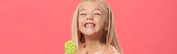 Plano panorámico de niño sonriente y lindo sosteniendo piruleta aislado en rosa - foto de stock