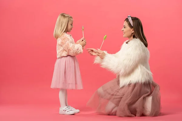 Vue latérale de la fille et de la mère souriante tenant des sucettes sur fond rose — Photo de stock