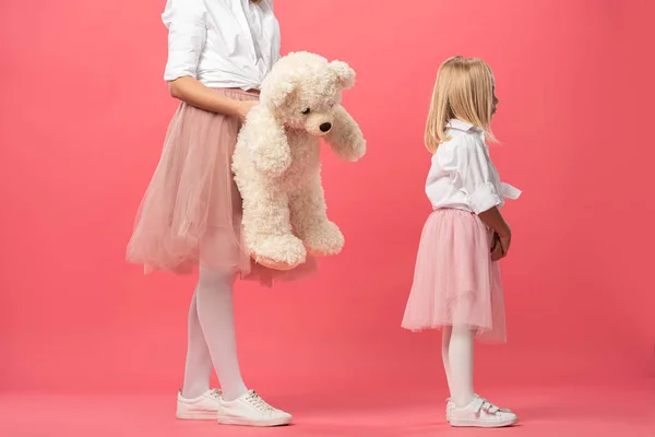Cropped view of mother giving teddy bear to offended daughter on pink background — Stock Photo