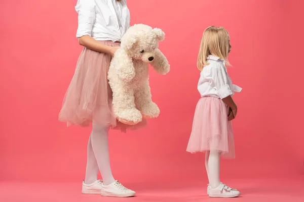 Vista recortada de la madre dando osito de peluche a la hija ofendida sobre fondo rosa - foto de stock