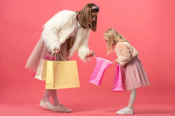 Shocked daughter and mother looking at shopping bag on pink background — Stock Photo