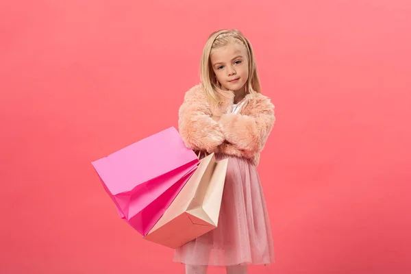 Cute kid with crosses arms holding shopping bags isolated on pink — Stock Photo