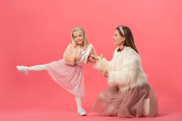 Daughter and smiling mother holding lollipops on pink background — Stock Photo