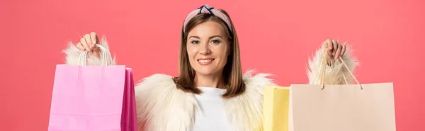 Panoramic shot of attractive and smiling woman holding shopping bags isolated on pink — Stock Photo