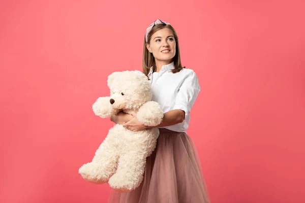 Attraente e sorridente donna tenendo orsacchiotto isolato su rosa — Foto stock