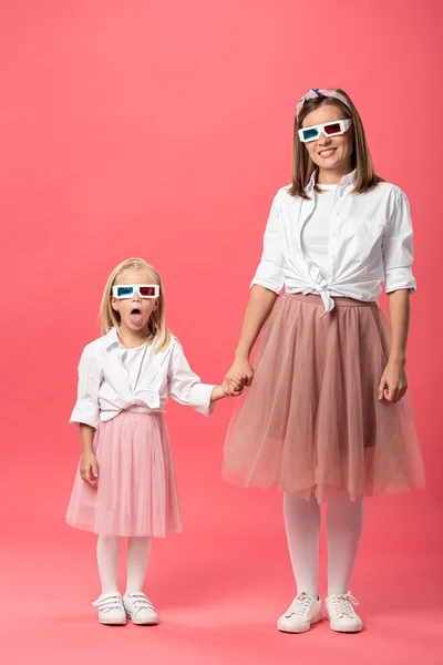 Daughter sticking out tongue and holding hands with mother in 3d glasses on pink background — Stock Photo