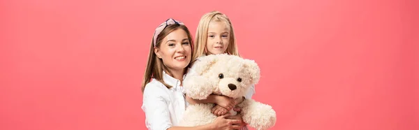 Panoramic shot of daughter and smiling mother with teddy bear isolated on pink — Stock Photo