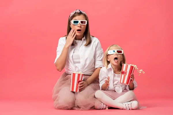 Chocado filha e mãe com 3d óculos segurando pipoca no fundo rosa — Fotografia de Stock