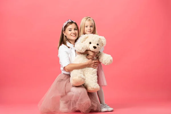 Daughter and smiling mother with teddy bear on pink background — Stock Photo