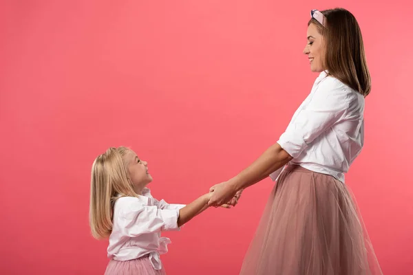 Seitenansicht von lächelnder Tochter und Mutter, die Hände isoliert auf rosa — Stockfoto