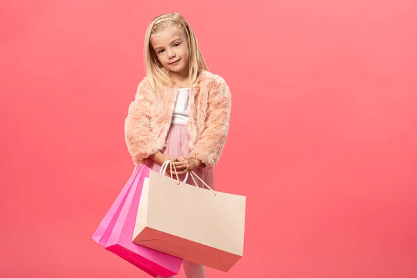 Lindo y sonriente niño sosteniendo bolsas aisladas en rosa - foto de stock