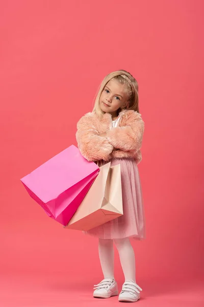 Mignon enfant avec les bras croisés tenant des sacs à provisions sur fond rose — Photo de stock