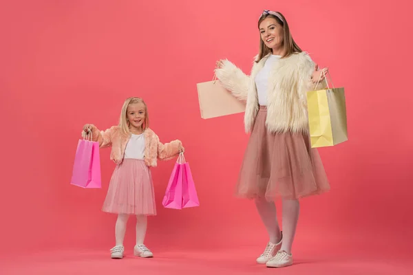 Улыбающаяся дочь и мать держат сумки для покупок на розовом фоне — стоковое фото