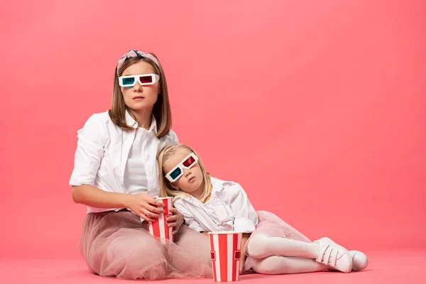 Soñolienta hija y madre en gafas 3d con palomitas de maíz sobre fondo rosa - foto de stock