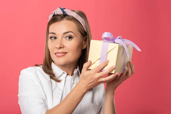 Attraktive und lächelnde Frau mit Geschenk isoliert auf rosa — Stockfoto