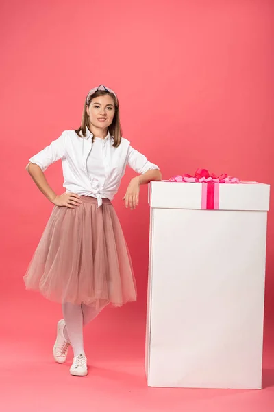 Attrayant et souriant femme debout près boîte cadeau sur fond rose — Photo de stock