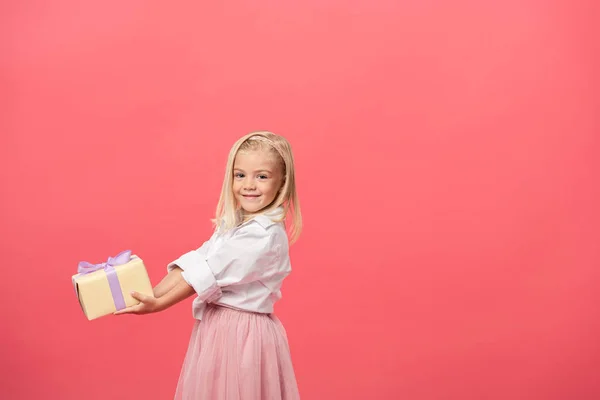 Lindo y sonriente niño sosteniendo regalo aislado en rosa - foto de stock