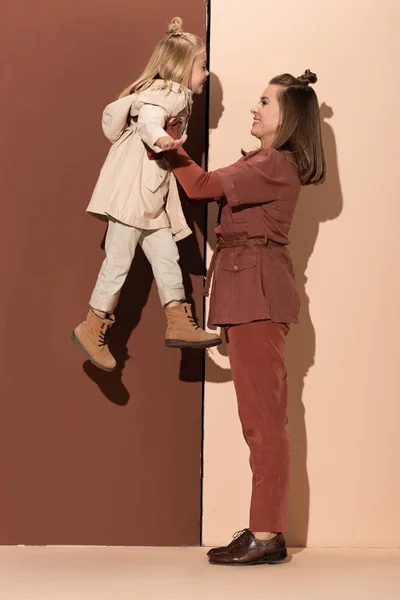 Вид збоку матері тримає усміхнену дочку на бежевому і коричневому фоні — стокове фото