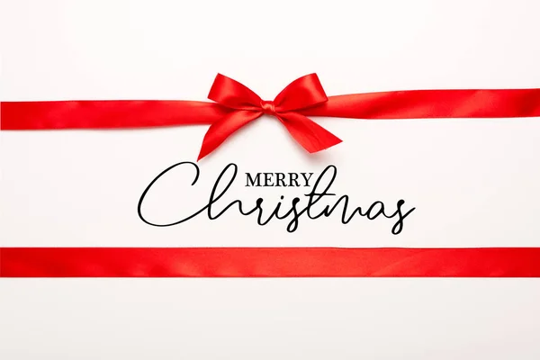 Draufsicht auf rotes Band und Schleife mit frohem Weihnachtsschriftzug auf weißem Grund — Stockfoto