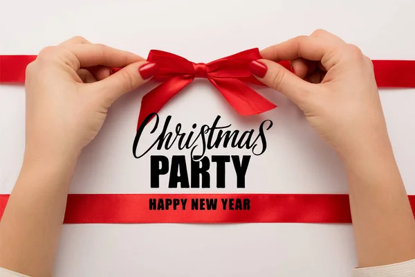 Cropped view of woman touching red bow near christmas party, happy new year lettering on white — Stock Photo