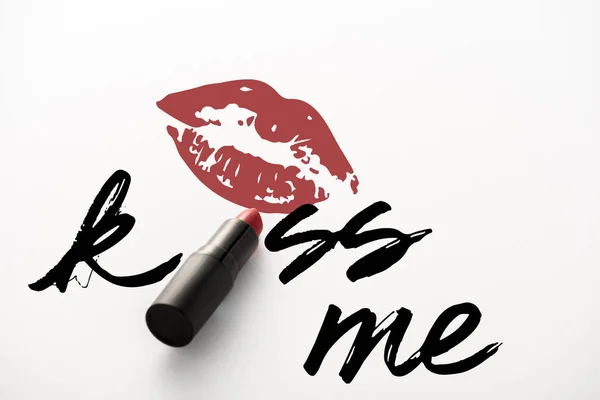 Black tube with red lipstick near kiss me letters and kiss print on white — Stock Photo
