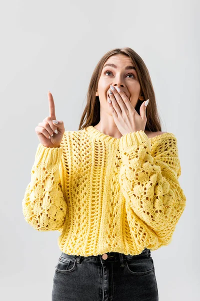 Shocked girl pointing with finger, covering mouth with hand and looking up isolated on grey — Stock Photo